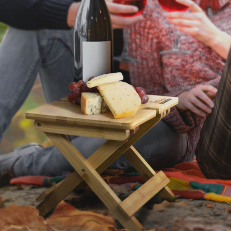 Stylish folding bamboo wine table for outdoor gatherings, holding two glasses with collapsible legs for easy transport.