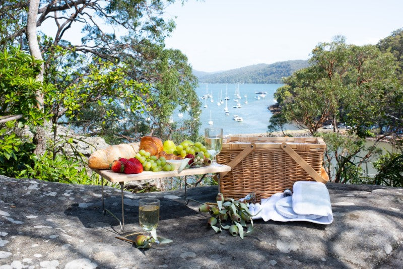 Insulated picnic basket for four, featuring a polished pine lid, organized utensils, and convenient drop handles for outdoor dining.