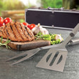 BBQ tool set in sleek metal case with stainless steel fork, tongs, and spatula, perfect for grilling enthusiasts.