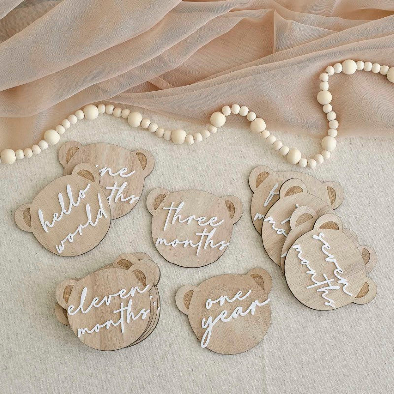 Wooden bear-shaped milestone signs for baby's first year, including "HELLO WORLD" and "ONE YEAR" with white acrylic lettering.