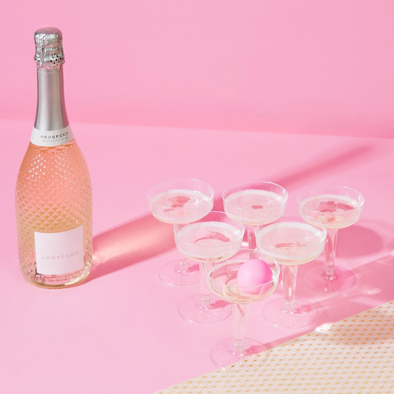 Prosecco Pong game set featuring 12 plastic glasses and 3 pink ping pong balls for trendy, bubbly party fun.