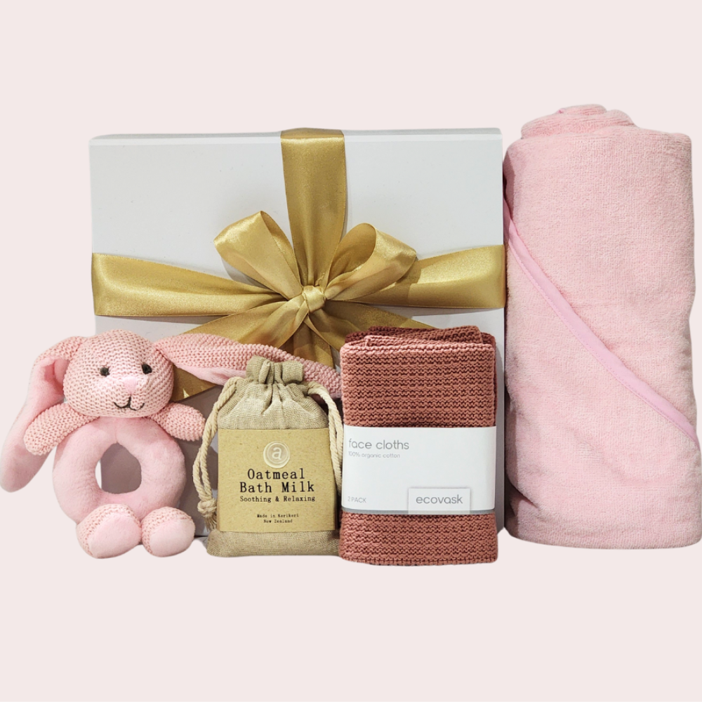 Blush Baby Essentials Gift Box featuring a soft hooded towel, bunny rattle, soothing bath milk, and luxurious facecloths.